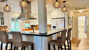 Une cuisine moderne dotée d’un îlot central, de tabourets de bar, de luminaires suspendus et d’une hotte de cuisine en acier inoxydable.