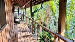 Une terrasse en bois dotée d’une rambarde, entourée d’une végétation tropicale luxuriante.