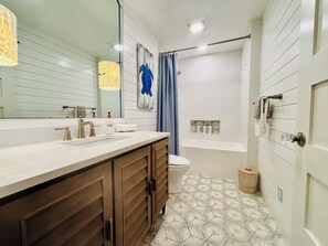 Une salle de bain avec un meuble-lavabo à deux vasques, des toilettes, une baignoire et un rideau de douche.