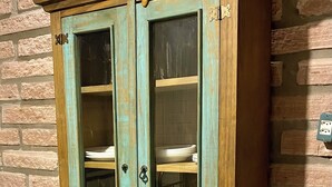 Un meuble de couleur bleu-vert, doté de deux portes et de deux tiroirs, placé contre un mur en briques.