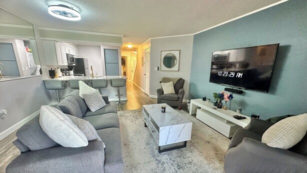 A modern living room with grey sofas, a coffee table, a TV, and a kitchen area in the background. - Work & Family Travel Friendly-Pool, Marina, Golf with Fee (Niceville)
