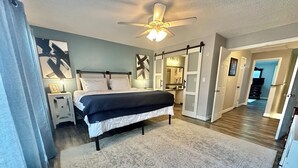 A bedroom with a bed, nightstands, a ceiling fan, and a hallway leading to a bathroom. - Work & Family Travel Friendly-Pool, Marina, Golf with Fee (Niceville)