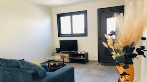Un salon moderne avec un canapé bleu, une table basse en verre, un téléviseur posé sur un meuble en bois et un vase décoratif contenant des plumes d’herbe des pampas.