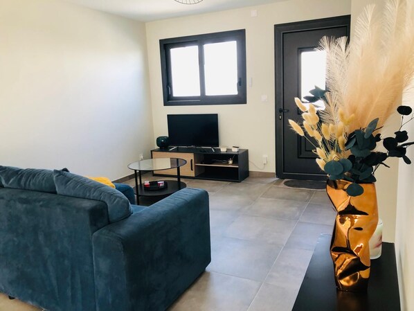 A modern living room with a blue sofa, a glass coffee table, a TV on a wooden stand, and a decorative vase with pampas grass.