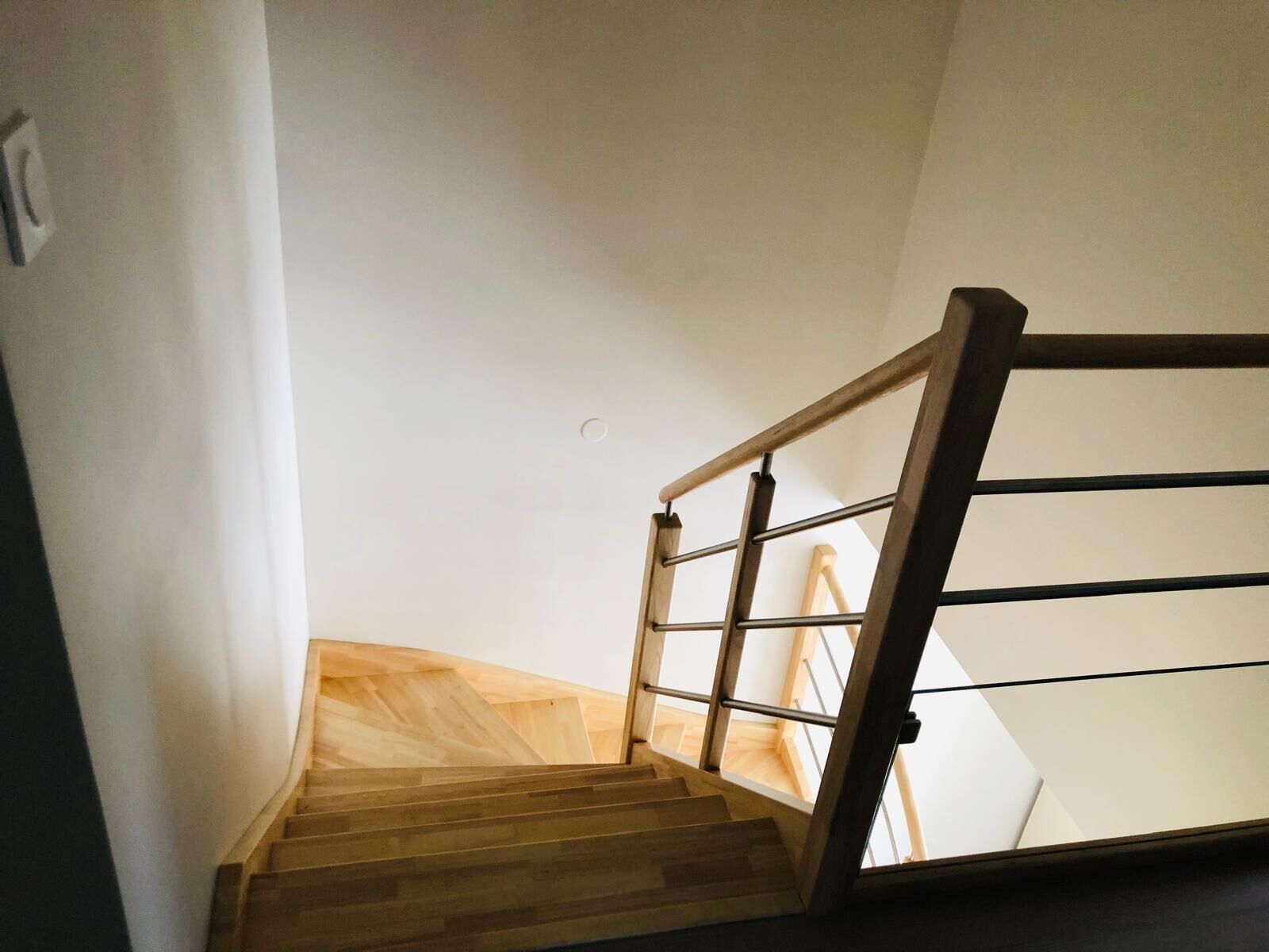 A wooden staircase with a metal handrail and a view of the upper floor.