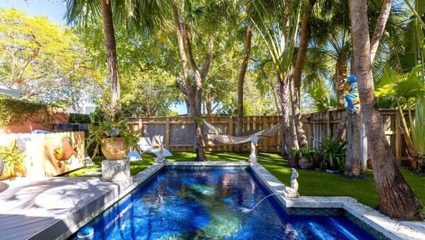 Patio con piscina, rodeado de palmeras y una hamaca.