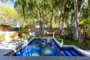 Un jardin avec une piscine, entouré de palmiers et agrémenté d’un hamac.
