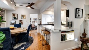 Una cocina moderna con armarios blancos, una isla central y un comedor con una mesa redonda y sillas azules.