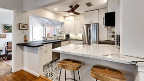 Una cocina moderna con armarios blancos, encimera de mármol y refrigerador de acero inoxidable.