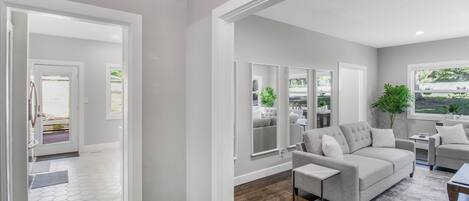 A modern living room with a grey sofa, a coffee table, and a view of the outdoors through large windows.