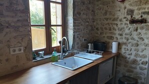 A kitchen with a wooden countertop, a sink, a window, a clock, and a stone wall.