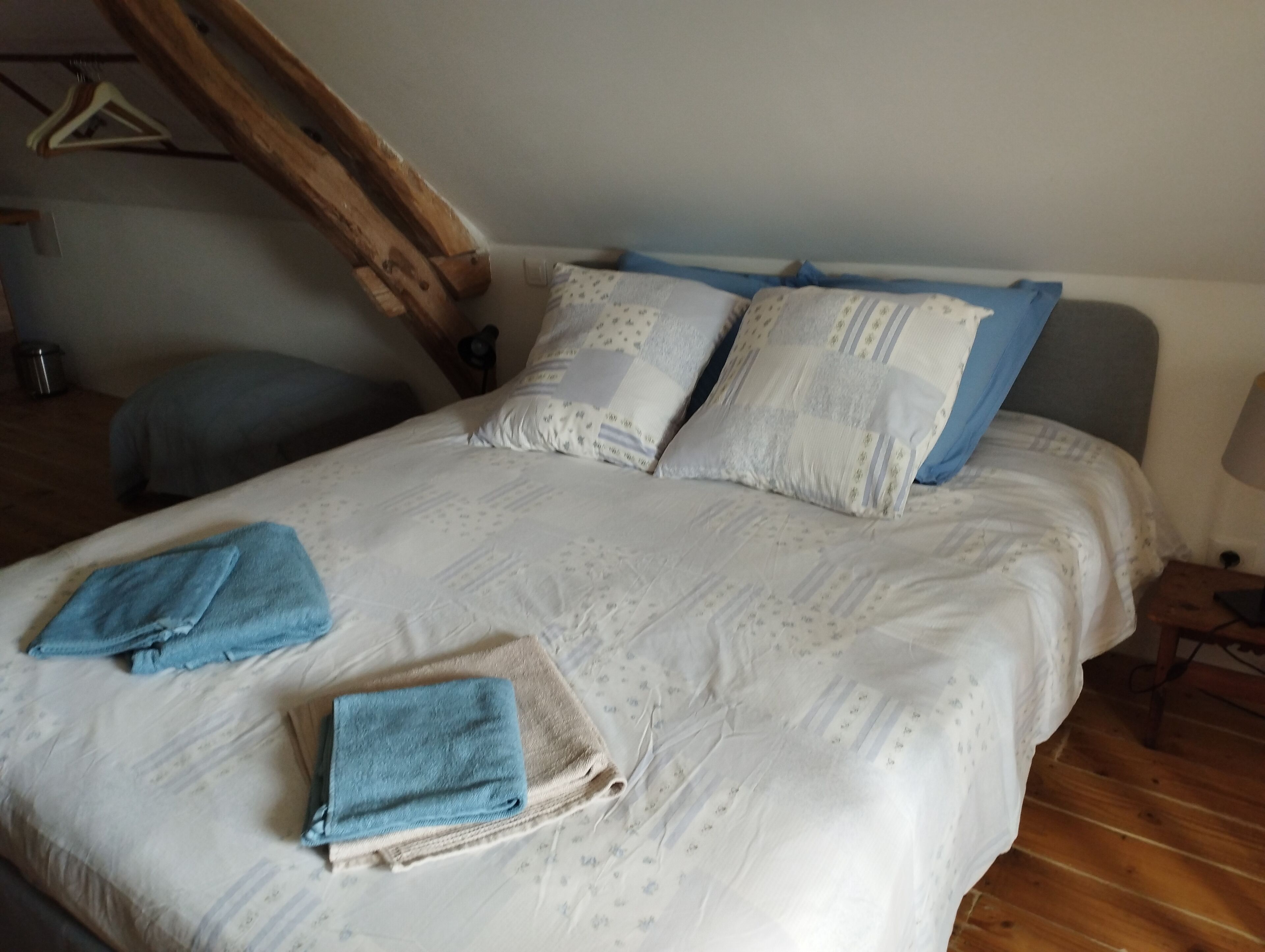 Una cama bien hecha con una colcha estampada, dos almohadas y toallas dobladas.
