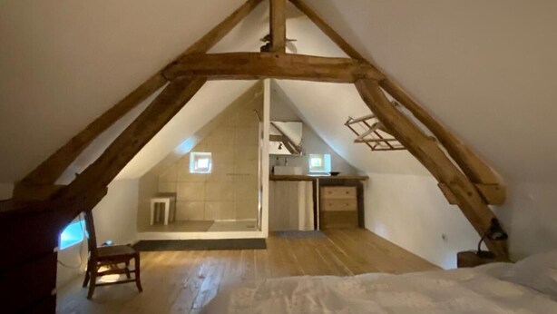 A room with a sloped ceiling and wooden beams, a small window, and a chair.