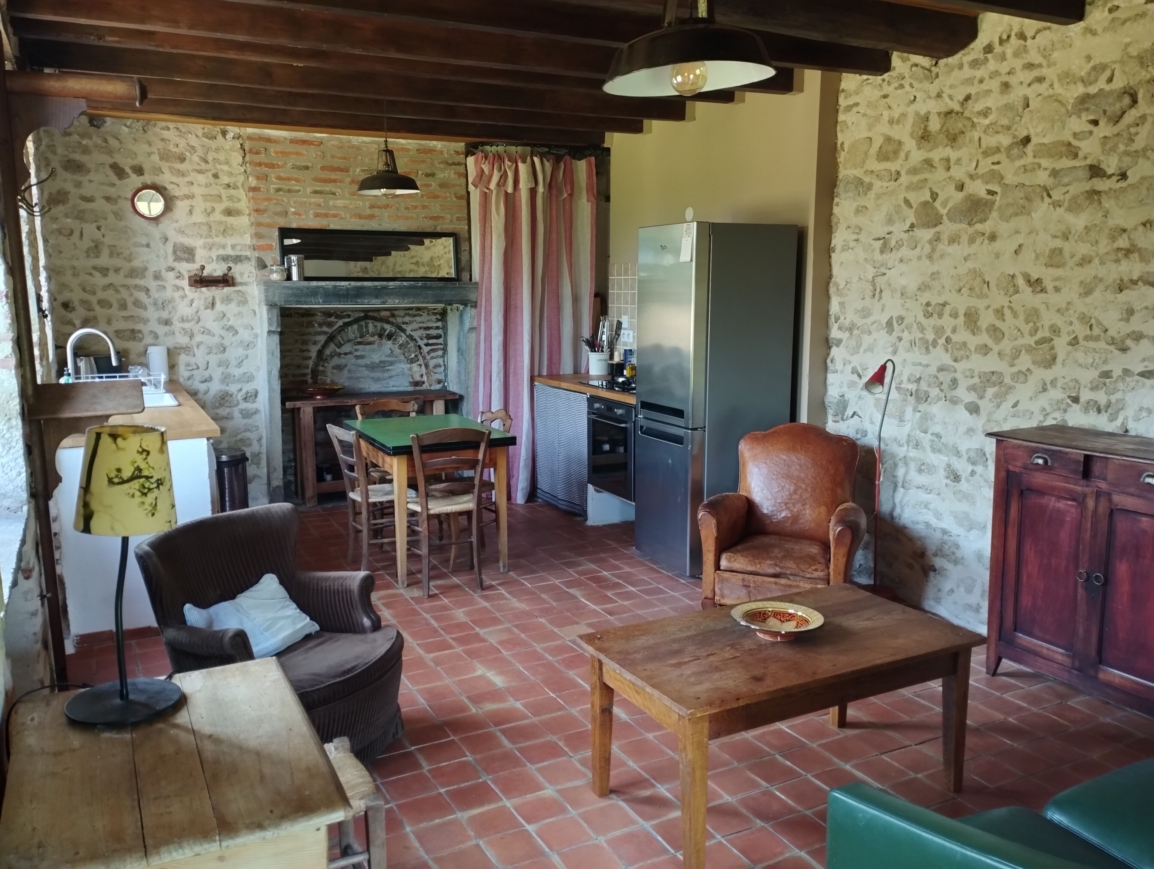 Une cuisine rustique avec un mur en briques, des meubles en bois, une table à manger et un réfrigérateur.