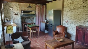 A rustic kitchen with a brick wall, wooden furniture, a dining table, and a refrigerator.