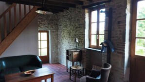 A rustic room with a wooden staircase, stone walls, a green sofa, a wooden table, and a window with a view.