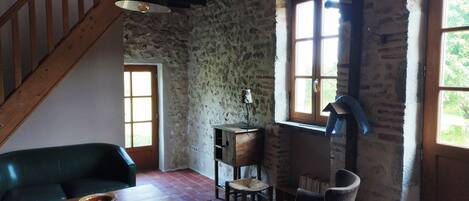 A rustic room with a wooden staircase, stone walls, a green sofa, a wooden table, and a window with a view.