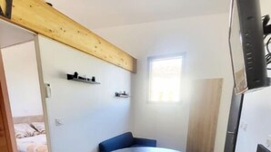 A compact room with a round table and chairs, a small window, and a bed in the background. - House sleeps 4 (Saint-Léger-sous-Brienne)