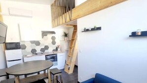 A compact kitchen with a dining area, a blue sofa, and a wooden staircase. - House sleeps 4 (Saint-Léger-sous-Brienne)
