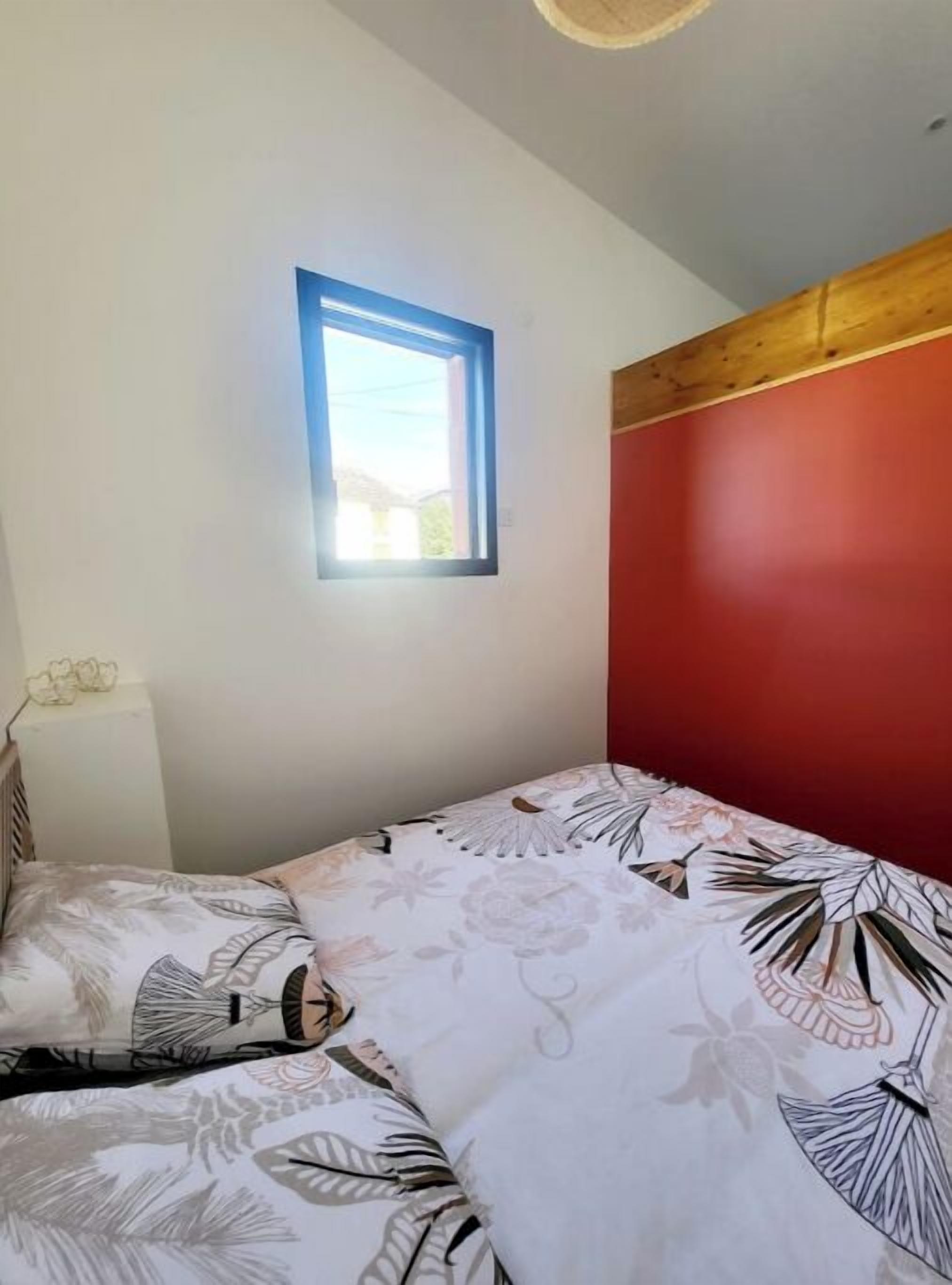 A bedroom with a bed, a window, and a red wall.