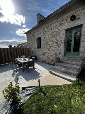 A stone building with a patio, a table with chairs, and a green door. - Family cottage in the countryside with private Nordic bath (Scaër)