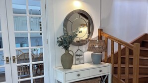 A white console table with a mirror, a vase, and a sign that reads 'Maison de Famille.'