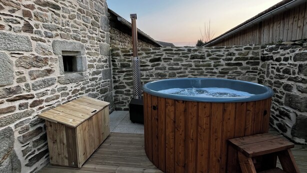 A wooden deck with a hot tub, a wooden bench, and a stone wall.