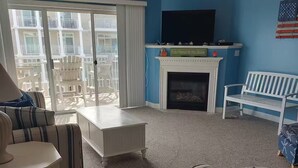 Ein Wohnzimmer mit Kamin, einem weißen Sofa, einem gestreiften Sessel und Blick auf den Balkon.