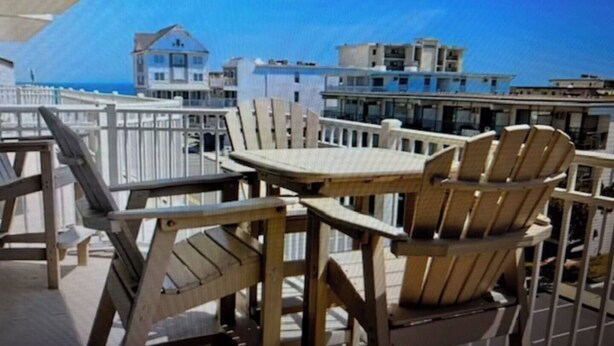 Eine Holzterrasse mit Tisch und Stühlen, mit Blick auf eine Küstenlandschaft mit Gebäuden und dem Meer.