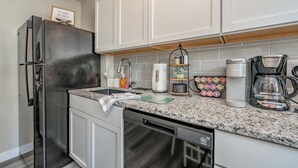 Una cocina moderna con armarios blancos, un refrigerador de acero inoxidable, una cafetera y un hervidor.