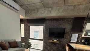 Un salon moderne avec un canapé gris, une table basse ronde et un coin cuisine doté d’un bar et de tabourets.