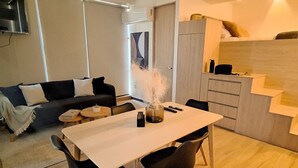 A modern living room with a sofa, a dining table, and chairs. There is a staircase leading to an upper level. - New apartment Nous 606 (Guadalajara)