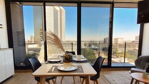 A dining area with a table set for two, large windows with a city view, and modern interior design. - New apartment Nous 606 (Guadalajara)