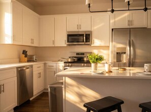 Una cocina moderna con armarios blancos, electrodomésticos de acero inoxidable, una isla central y una pequeña planta en maceta.