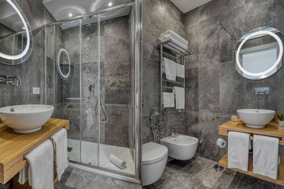 A modern bathroom with a glass-enclosed shower, two sinks, a bidet, and a toilet.