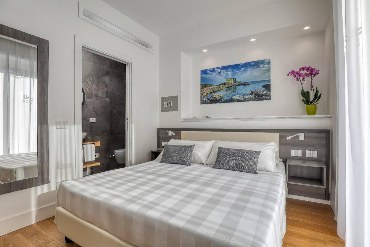 A modern bedroom with a large bed, a headboard with built-in lighting, a painting above the bed, and a small potted plant.