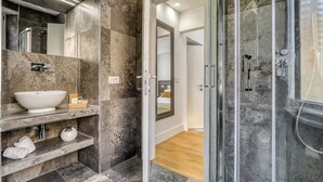A modern bathroom with a large sink, mirror, and shower area. - Gallery Suite (Civitavecchia)