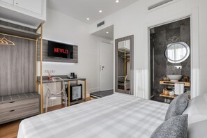 A modern hotel room with a bed, a desk with a computer, a TV displaying 'NETFLIX', a wardrobe, a bathroom with a mirror and sink, and a round mirror. - Gallery Suite (Civitavecchia)