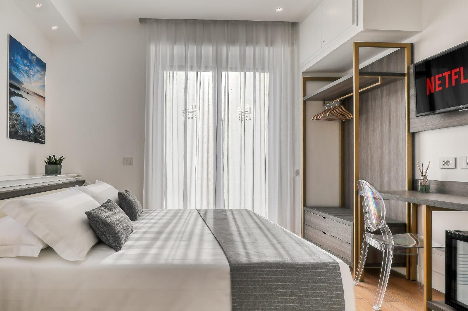 Un dormitorio moderno con una cama, un escritorio, una silla y un televisor mostrando el logotipo de Netflix.