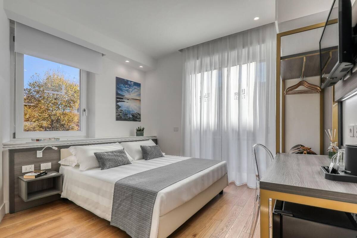 A modern bedroom with a large bed, bedside tables, a desk, and a window with a view of trees.