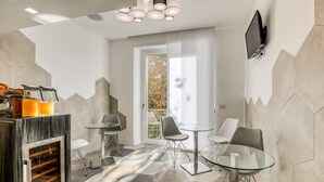 A modern bathroom with a glass shower, a breakfast bar with orange juice, and a seating area with chairs and a table. - Gallery Suite (Civitavecchia)