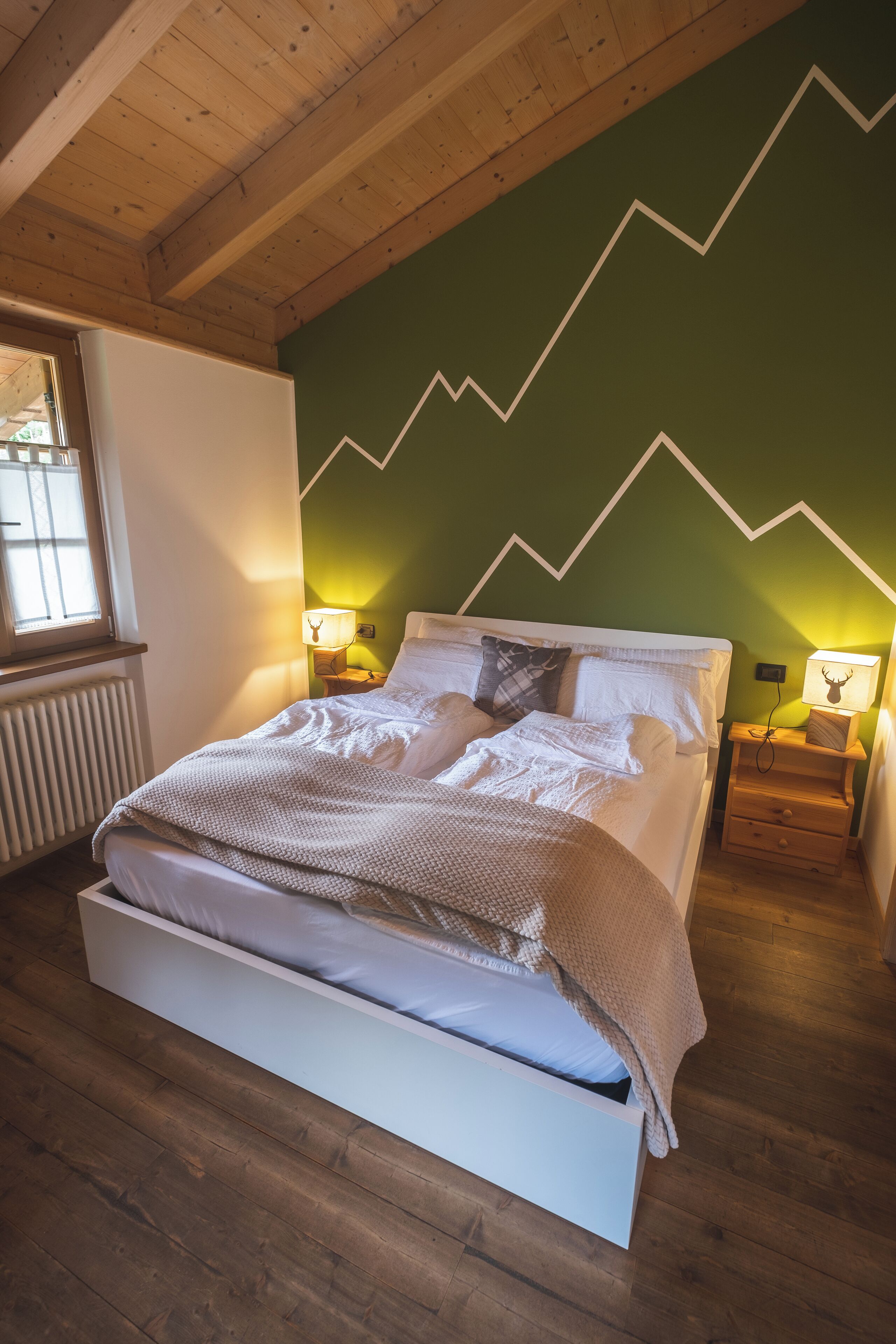 A bedroom with a bed, two bedside tables, a window, and a green wall with a zigzag pattern.