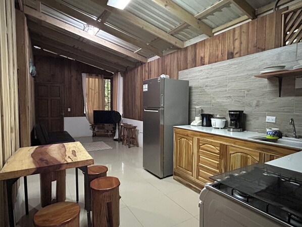 A kitchen with wooden cabinets, a refrigerator, a stove, and a dining area with stools.