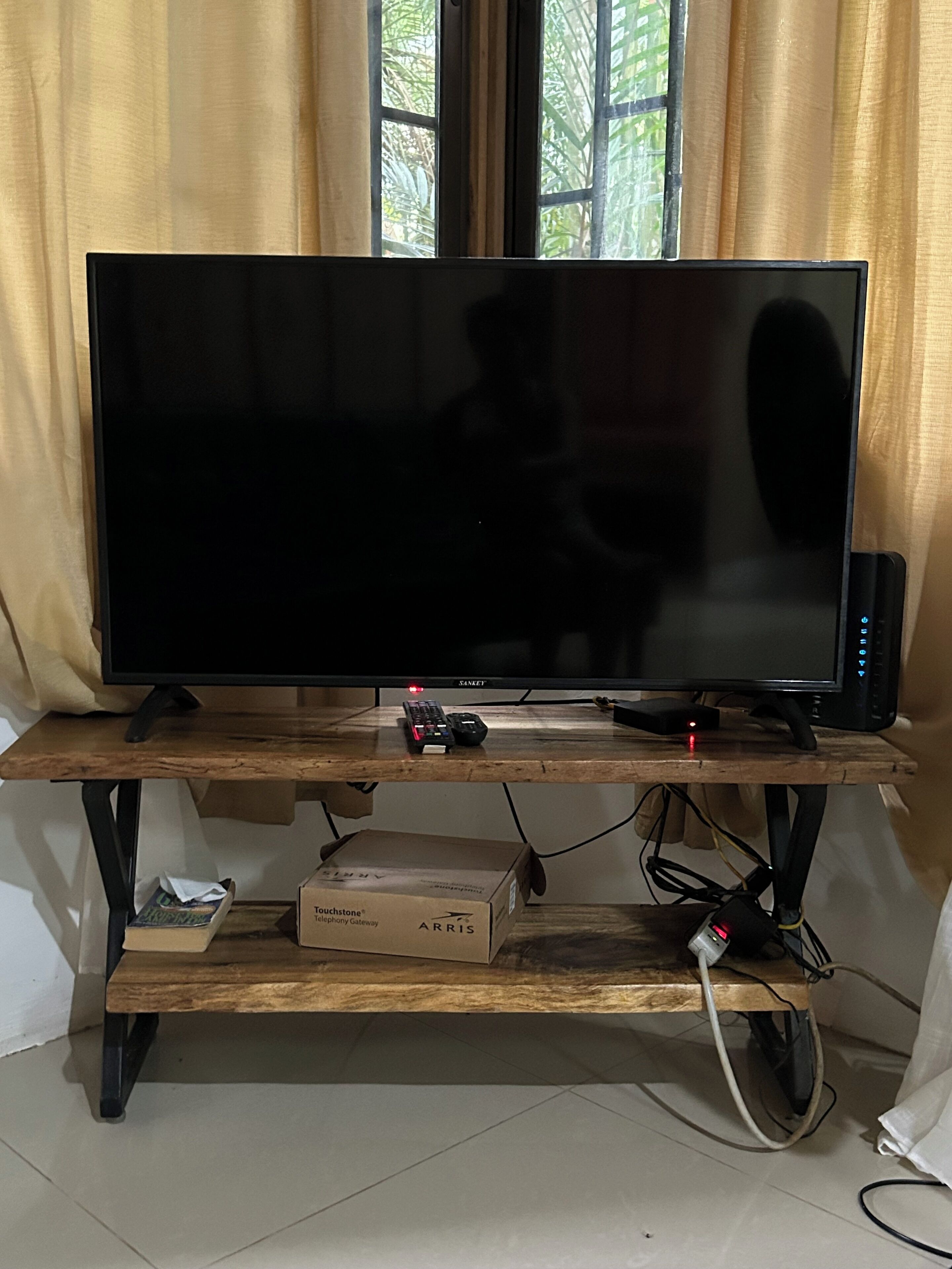 En tv-apparat står på ett träställ. En fjärrkontroll ligger framför den, och under tv:n finns en låda med texten ”Touchstone Telephony Gateway”.