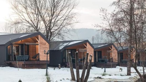 A row of wooden cabins with large windows and a covered porch, situated in a snowy landscape with a calm pond in the foreground. - Halicanum Glamping Peaceful Retreat Resort (Sveti Martin na Muri)