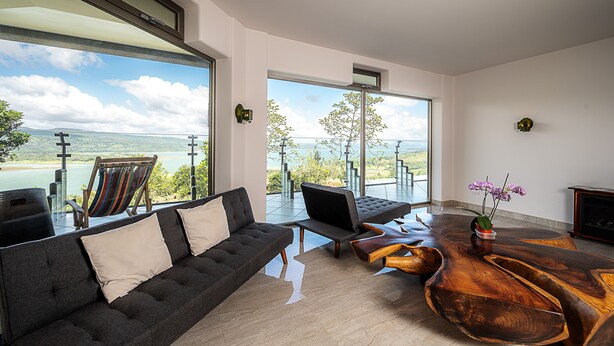 Un salon moderne avec une grande fenêtre, un canapé, une table basse et une vue sur un lac.