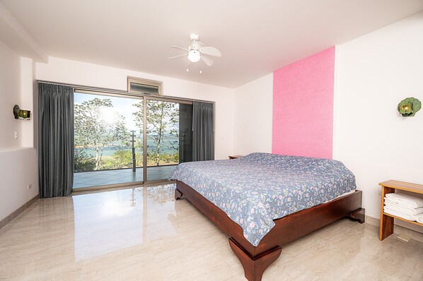 A bedroom with a large bed, a ceiling fan, a view through a sliding door, and a pink accent wall.