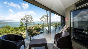 Un balcon agrémenté de meubles en osier, d’une table en verre et offrant une vue sur un lac et des montagnes.
