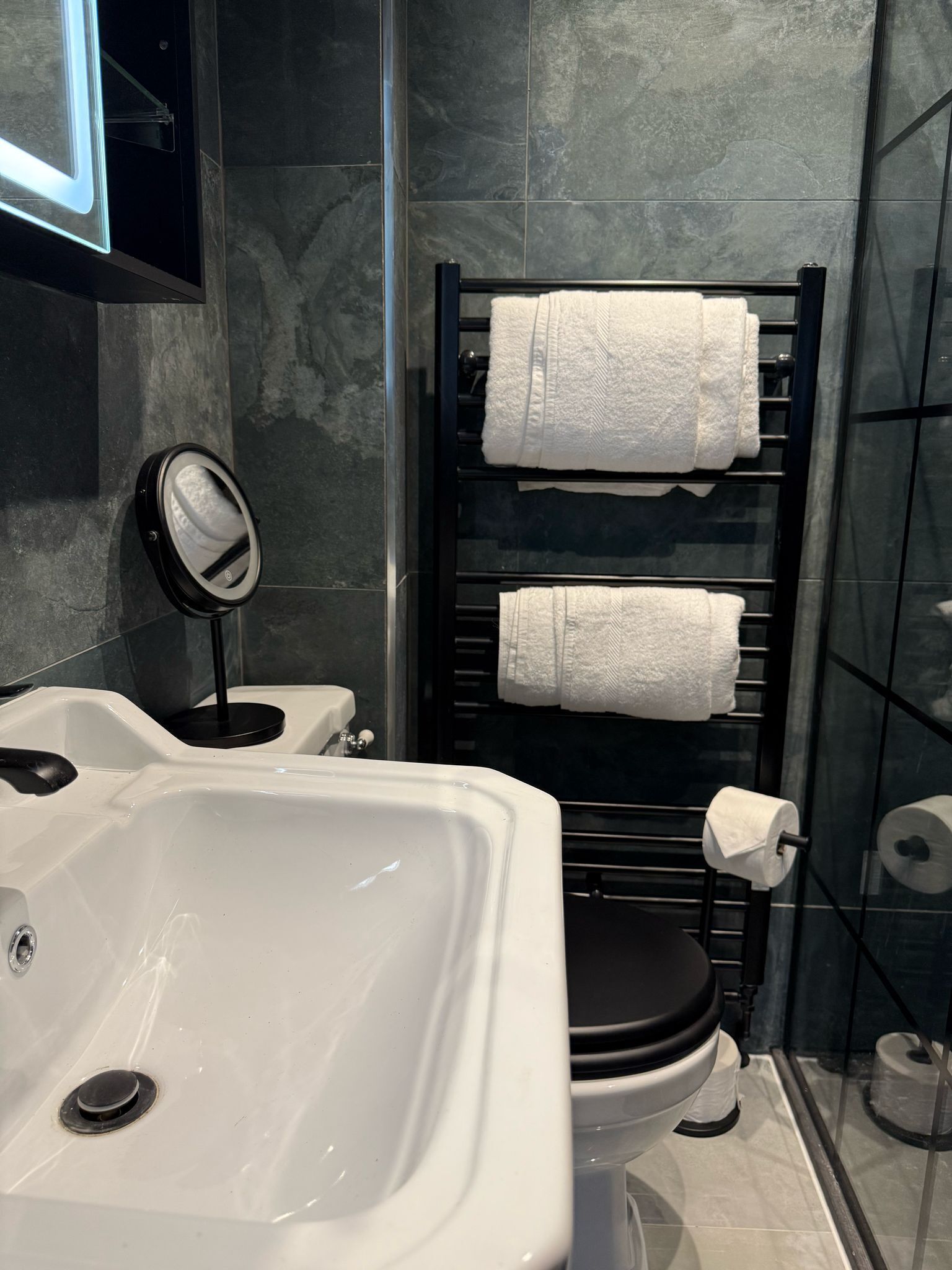 Un baño con un lavabo blanco, un inodoro negro y un toallero con dos toallas blancas.