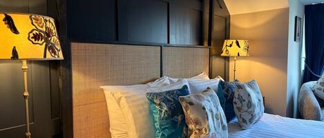Una habitación de hotel con una cama grande, un cabecero de textura tejida y dos lámparas de noche con motivos florales.